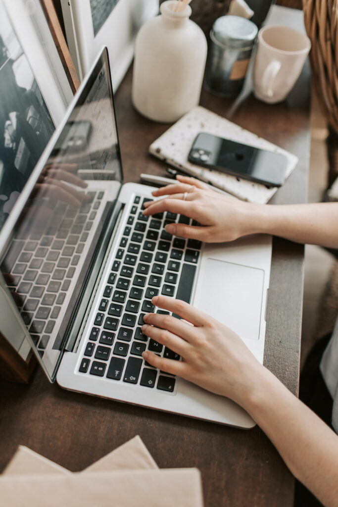 person typing on laptop with phone and notebook on the side 