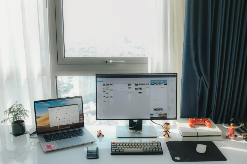 laptop on desk with a desktop on desk with some toys and a small plant